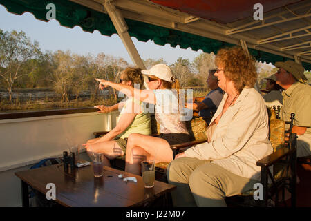 Les personnes bénéficiant d'une croisière au coucher du soleil, avec une femme pointant sur un animal à terre, sur le Zambèze, le Zimbabwe, l'Afrique Banque D'Images