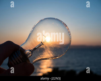 Man holding Light bulb contre le soleil au coucher du soleil Banque D'Images