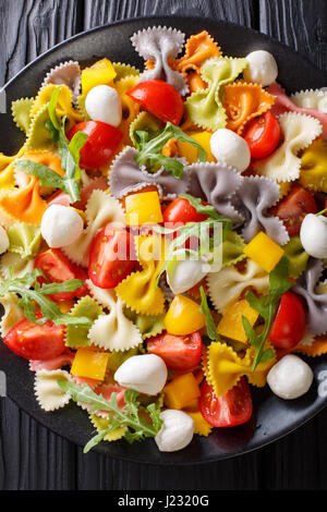 Pâtes farfalle multicolores avec des tomates et mozzarella gros plan sur la table. Vue verticale d'en haut Banque D'Images