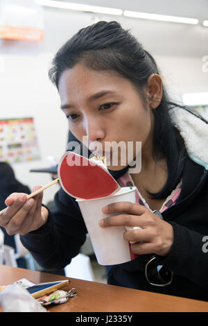 Jeune femme de manger des aliments à partir d'une tasse de papier dans la salle à manger dans le magasin.Asian girl eating lunch avec noodle à table dans la restauration rapide. Banque D'Images