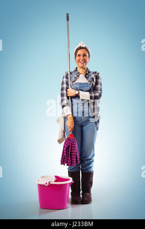 Cheerful woman with mop et du godet prêt à nettoyer le plancher sur fond bleu Banque D'Images