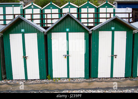 Lignes d'uniforme vert et blanc traditionnel, peint des cabines de plage sur une plage britannique avec des verrous sur leurs portes. Banque D'Images