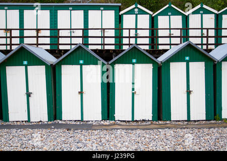 Lignes d'uniforme vert et blanc traditionnel, peint des cabines de plage sur une plage britannique avec des verrous sur leurs portes. Banque D'Images