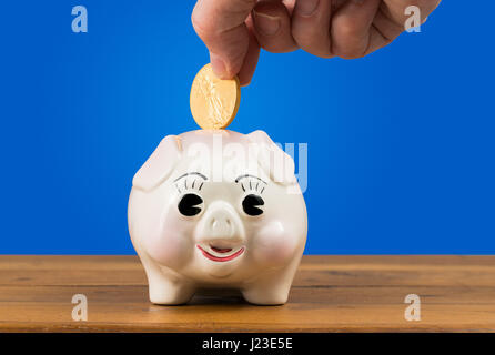 Tirelire avec une main mise dans une pièce d'or - concept d'épargne ou de placement Banque D'Images