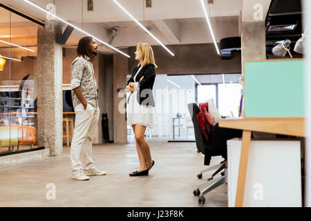 Colleagues talking in a modern office avant de s'asseoir à leur bureau. Banque D'Images