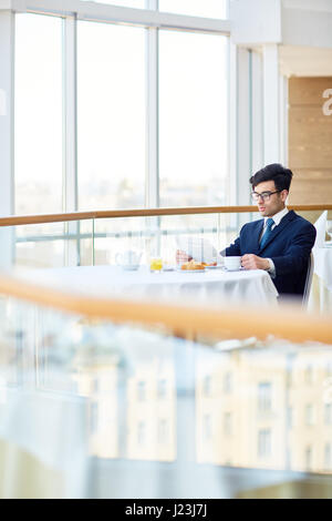Businessman se concentrant sur la lecture des nouvelles alors que sitting in restaurant Banque D'Images