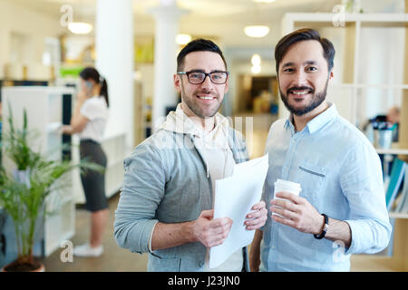 Portrait de deux professionnels modernes looking at camera et smiling standing dans open office space Banque D'Images