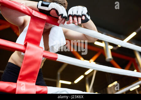 Low angle view of épuisé boxer s'appuyant sur les cordes avec anneau de serviette sur les épaules après une dure lutte Banque D'Images