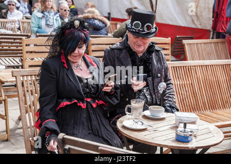 Un homme et une femme s'habiller pour le Whitby Goth célébrations prennent une pause et s'asseoir pour boire un verre et fumer et regarder leurs téléphones Banque D'Images