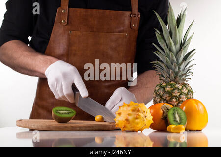 Les mains du chef, couper des fruits en morceaux sur une planche en bois Banque D'Images