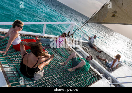 Groupe de touristes masculins et féminins ayant un verre alors que sur une croisière en catamaran au coucher du soleil au large de la côte d'Aruba, des Caraïbes. Banque D'Images