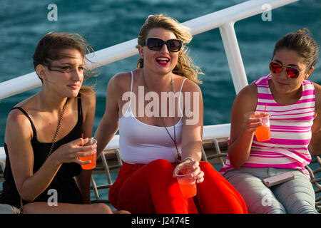 Groupe de touristes masculins et féminins ayant un verre alors que sur une croisière en catamaran au coucher du soleil au large de la côte d'Aruba, des Caraïbes. Banque D'Images