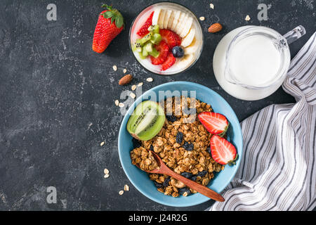 Petit-déjeuner sain : muesli, yaourt, fraises, banane, kiwi et pot de lait sur fond noir en ardoise. Vue de dessus, copiez l'espace. Concept de manger sain Banque D'Images