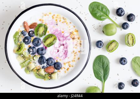 Bol à smoothie acai, kiwi, bleuets, amandes, noix de coco, du pollen d'abeille et bébés épinards sur fond blanc. Vue de dessus de désintoxication sain smoothy Banque D'Images