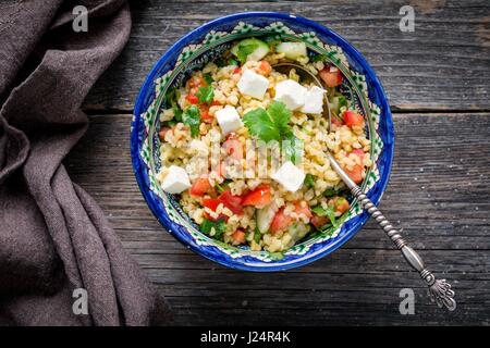 Taboulé salade avec du fromage blanc et de graines de grenade dans un bol sur fond de bois. Vue d'en haut Banque D'Images