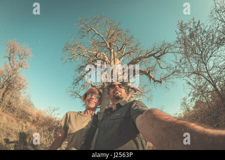 Couple près de l'usine selfies Baobab dans la savane africaine avec ciel bleu clair. Fisheye Vue de dessous, la tonalité de l'image. Wilderness Safari et avènement Banque D'Images