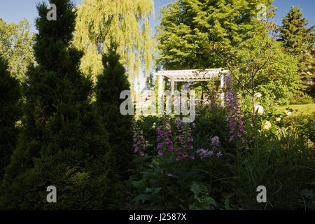 Vue d'une pergola à travers un lit de fleur dans un jardin résidentiel paysagé au printemps Banque D'Images
