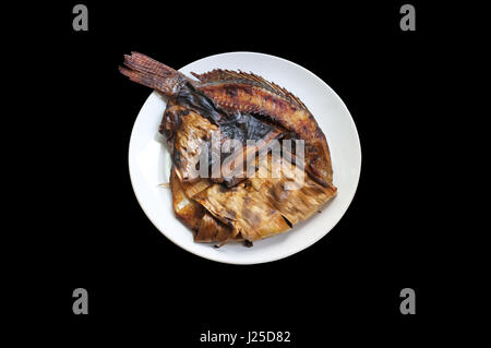 Une cuisine traditionnelle thaï , Poêle Grill poisson envelopper dans des feuilles de banane thai style sur fond noir Banque D'Images