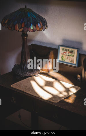 La lumière d'une fenêtre sur petit bureau avec lampe dans l'ombre Banque D'Images