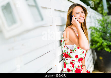 Belle jeune femme heureuse sourire lors d'un appel téléphonique alors qu'appuyé contre un mur blanc Banque D'Images