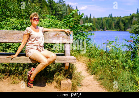 Portrait d'une femme se détendre sur un banc près de la rivière Banque D'Images