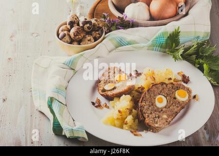 Vintage photo horizontale avec portion de viande faits maison à base de porc et de boeuf de la viande hachée et remplis par des oeufs de cailles sur plaque blanche avec pommes de maillé Banque D'Images