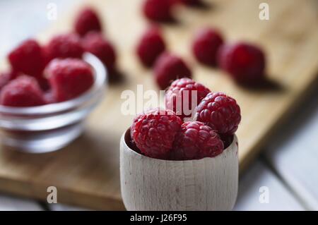 Framboises fraîches et légèrement imparfait dans petit bol en bois, plus de fruits rouges en arrière-plan. Banque D'Images