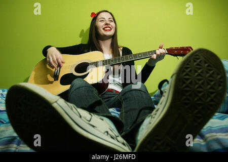 Jeune brunette rire et jouer la guitare sur le lit. Banque D'Images