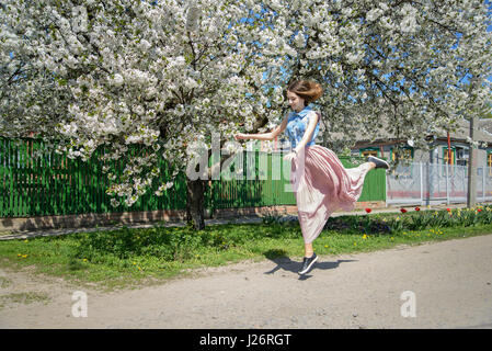 Une jeune fille court, rebondir dans le contexte d'un cerisier en fleurs Banque D'Images