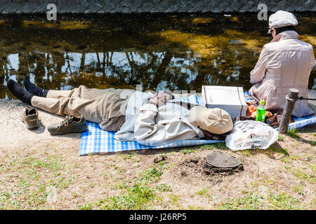 Le Japon, Shukugawa. Après quelques pique-nique sur rivière, femme à l'aide de son téléphone portable, l'homme endormi sur son dos avec chapeau sur le visage. Banque D'Images