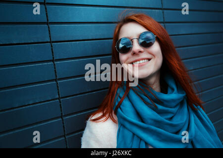 Hipster redhaired girl à lunettes élégant et manteau est posant devant un mur noir dans la rue Banque D'Images