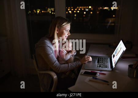 Mère avec son fils dans les bras, working on laptop Banque D'Images