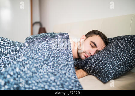 Jeune homme séduisant dormir confortablement au lit Banque D'Images