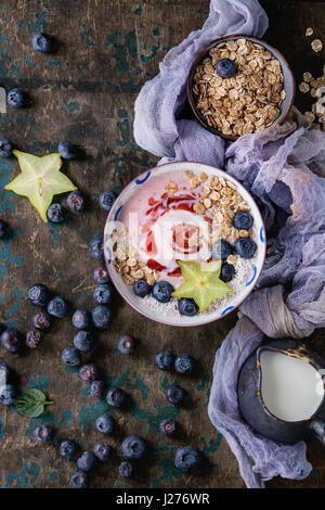 Bol à smoothie déjeuner sain. Yogourt aux fraises avec des bleuets, granola, menthe, pichet de lait et carambole sur plus de gaze textile en bois textur Banque D'Images