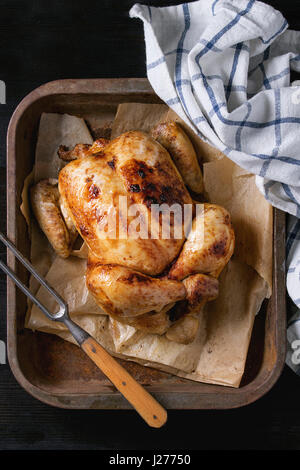 Tout cuit grillé poulet biologique sur support papier dans le vieux four plateau avec cuisine blanche serviette et fourchette à viande sur fond de bois brûlé noir. Top v Banque D'Images