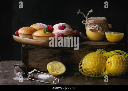 Muffin citron maison cupcakes avec les framboises, le sucre en poudre, menthe, servi avec un pot de lait caillé de citron et citrons sur boîte en bois sur fond sombre Banque D'Images