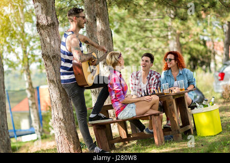 Mec tatoué avec guitare et chants donne de la joie à son ami en summer camp tandis que des boissons Bière Banque D'Images