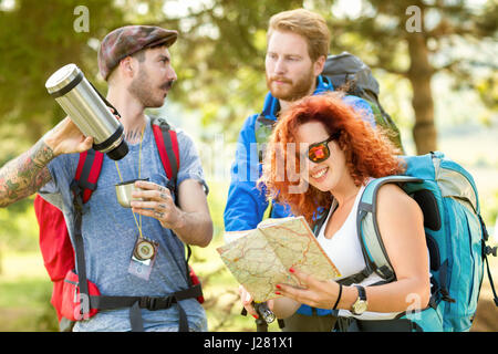 Tattooed man servi le café de thermos tandis que les femmes regarder map in woods Banque D'Images