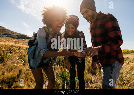 Groupe de randonneurs regardant des images sur téléphone mobile et rire. Heureux les jeunes de la randonnée dans la campagne. Banque D'Images