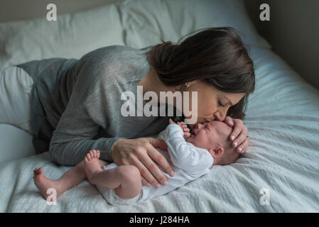 High angle view of mother kissing pleurer bébé nouveau-né garçon sur le front au lit Banque D'Images