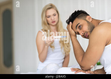 Young Couple Sitting in Bed, Woman Show Man Test de grossesse positif des relations de conflit, problème triste émotions négatives Chambre des Amoureux Banque D'Images