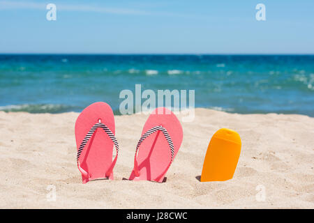 Bouteille d'écran solaire et rose tongs sur la plage Banque D'Images