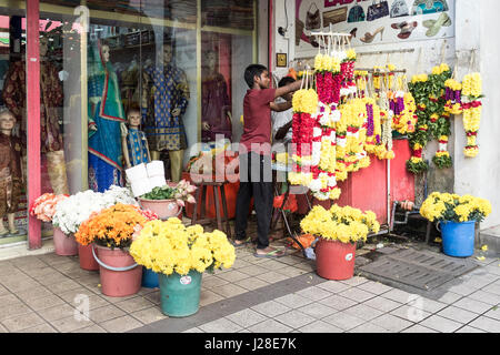Un commerçant tend son étal de fleurs au centre-ville de Kuala Lumpur, Malaisie, en tant que regard sur des mannequins d'une vitrine. Banque D'Images