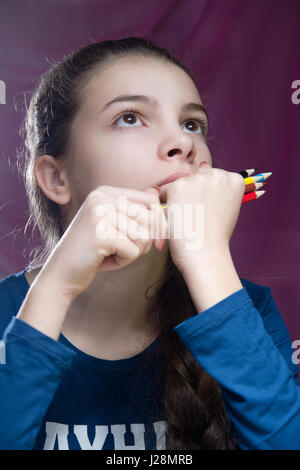 Portrait de fille charmante qui tient les crayons et recherche. Photo couleur vertical. Sur un fond rose Banque D'Images