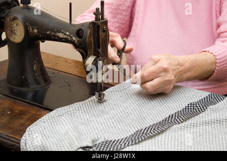 Une vieille femme aux cheveux blancs coud sur une vieille machine à coudre. L'adaptation d'une vieille femme couturière aux mains d'une vieille femme couturière la coupe d'un thread à la Banque D'Images