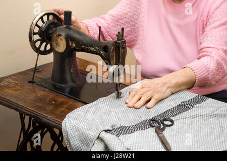 Une vieille femme aux cheveux blancs coud sur une vieille machine à coudre. L'adaptation d'une vieille femme couturière aux mains d'une vieille femme couturière la coupe d'un thread à la Banque D'Images