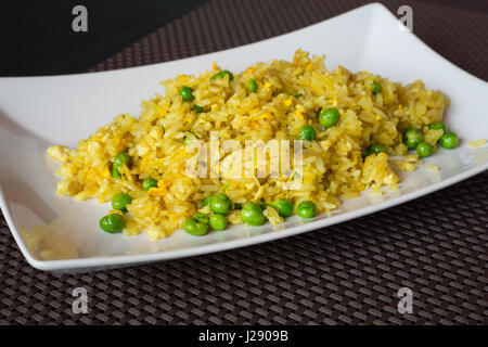 Poêlée de riz au curry avec pois servi sur assiette blanche au restaurant, fond brun. Banque D'Images