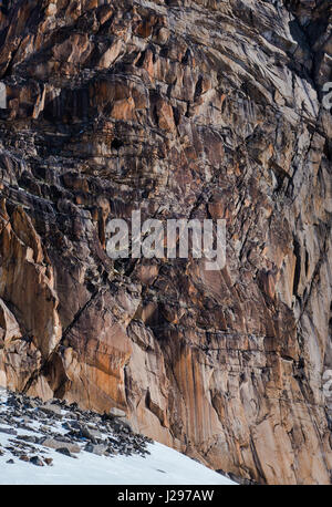 Falaise de granit érodés mur avec de multiples fissures dans différents tons de rouge et gris fer et plaques de neige en hiver Banque D'Images