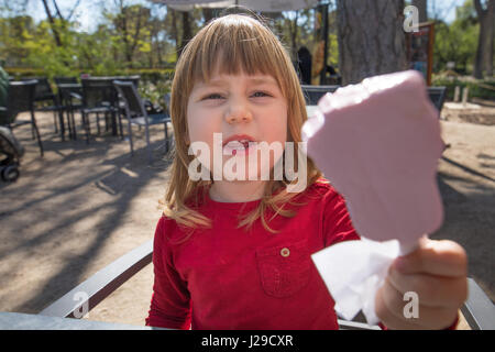 Portrait de trois ans de l'enfant blond rose offre lolly de glace ou de glace, assis à une terrasse de café bar avec table gris en stationnement Banque D'Images
