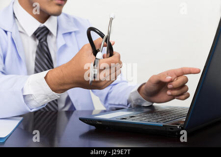 Homme médecin, médecin en blouse blanche holding stethoscope pointant à l'écran de l'ordinateur montrant quelque chose dans une clinique médicale Banque D'Images
